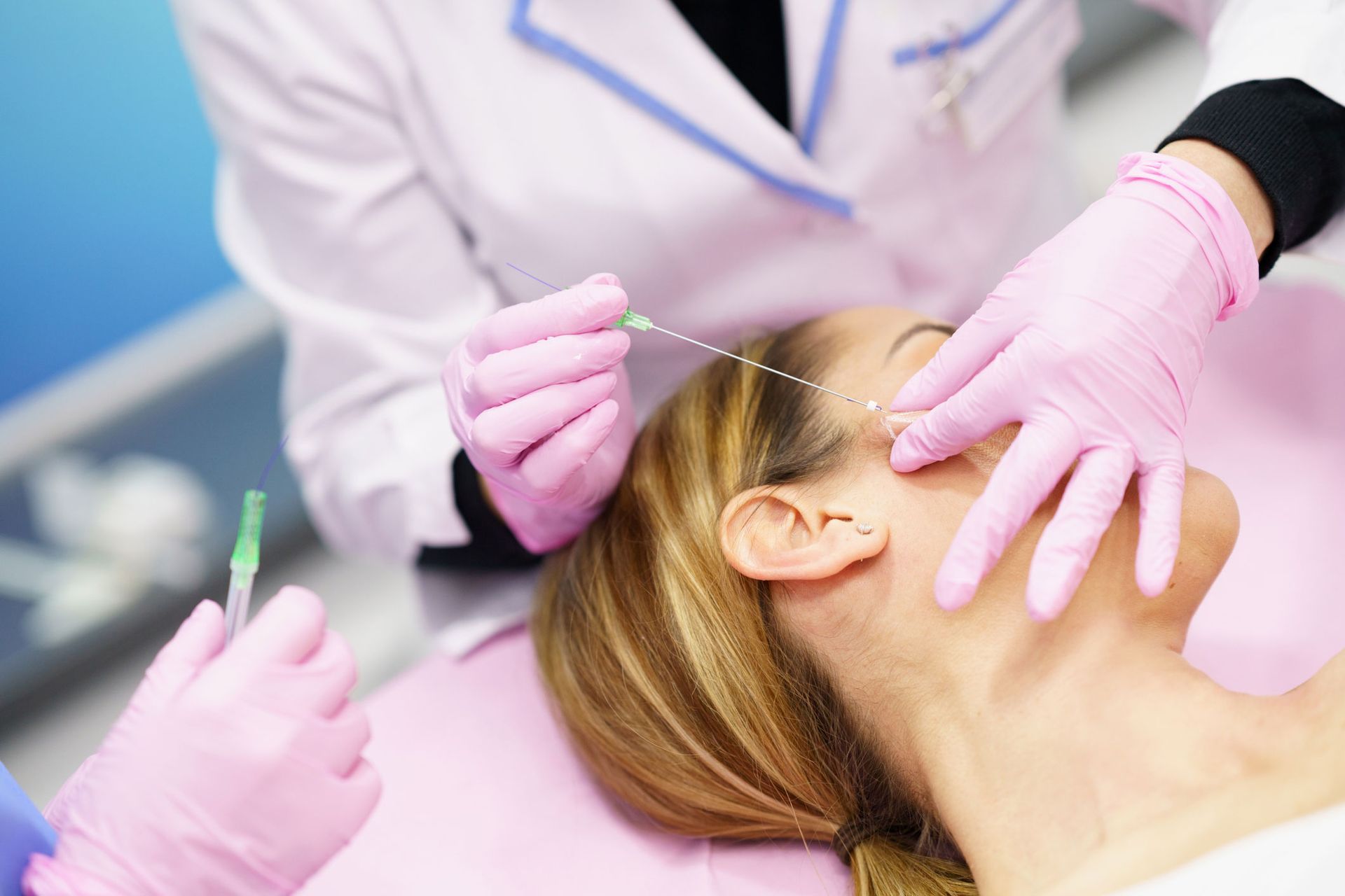 Woman receiving cosmetic procedure with thread, in clinic, medical staff in pink gloves.