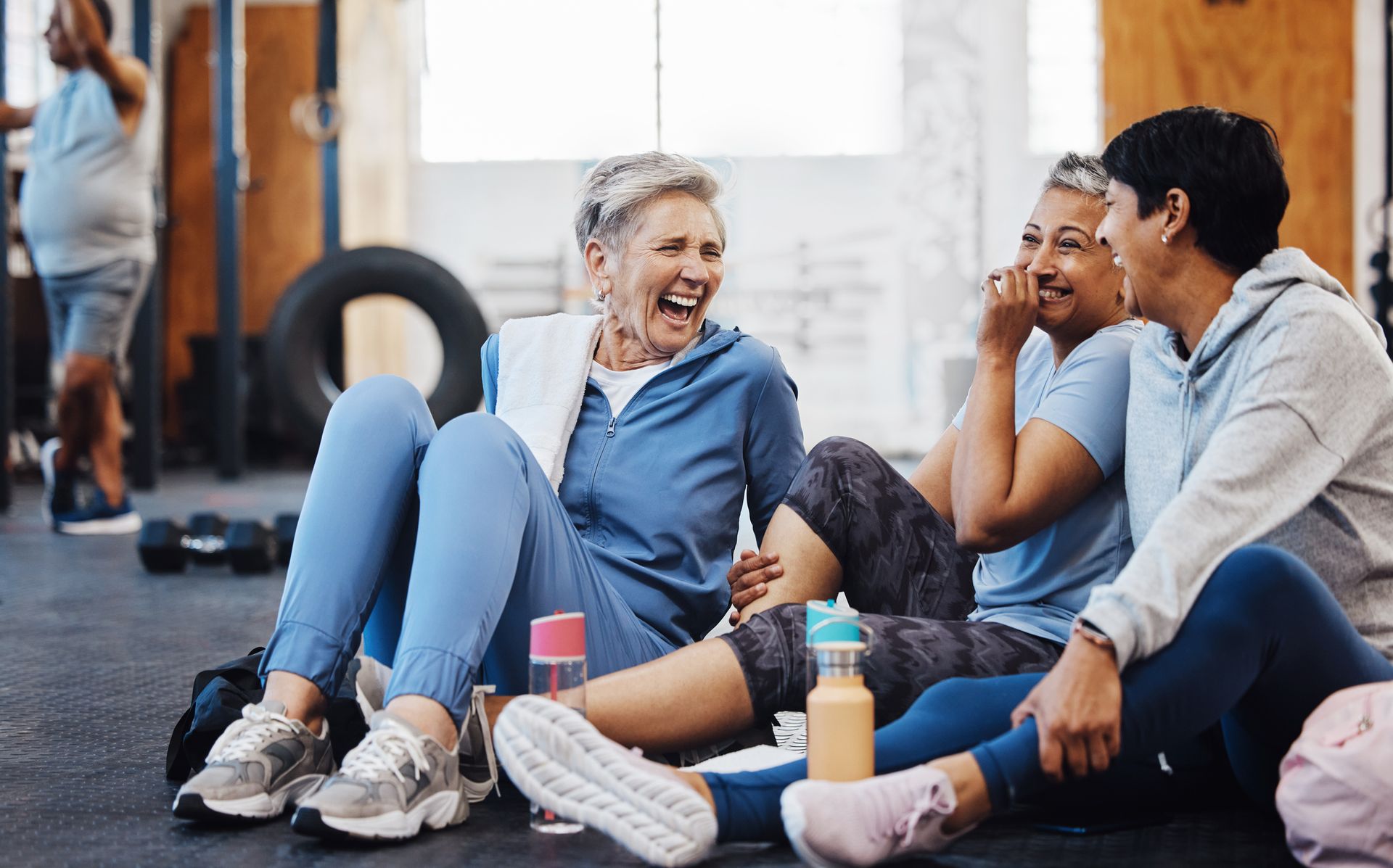Group of people in workout clothes laughing together on a gym floor.