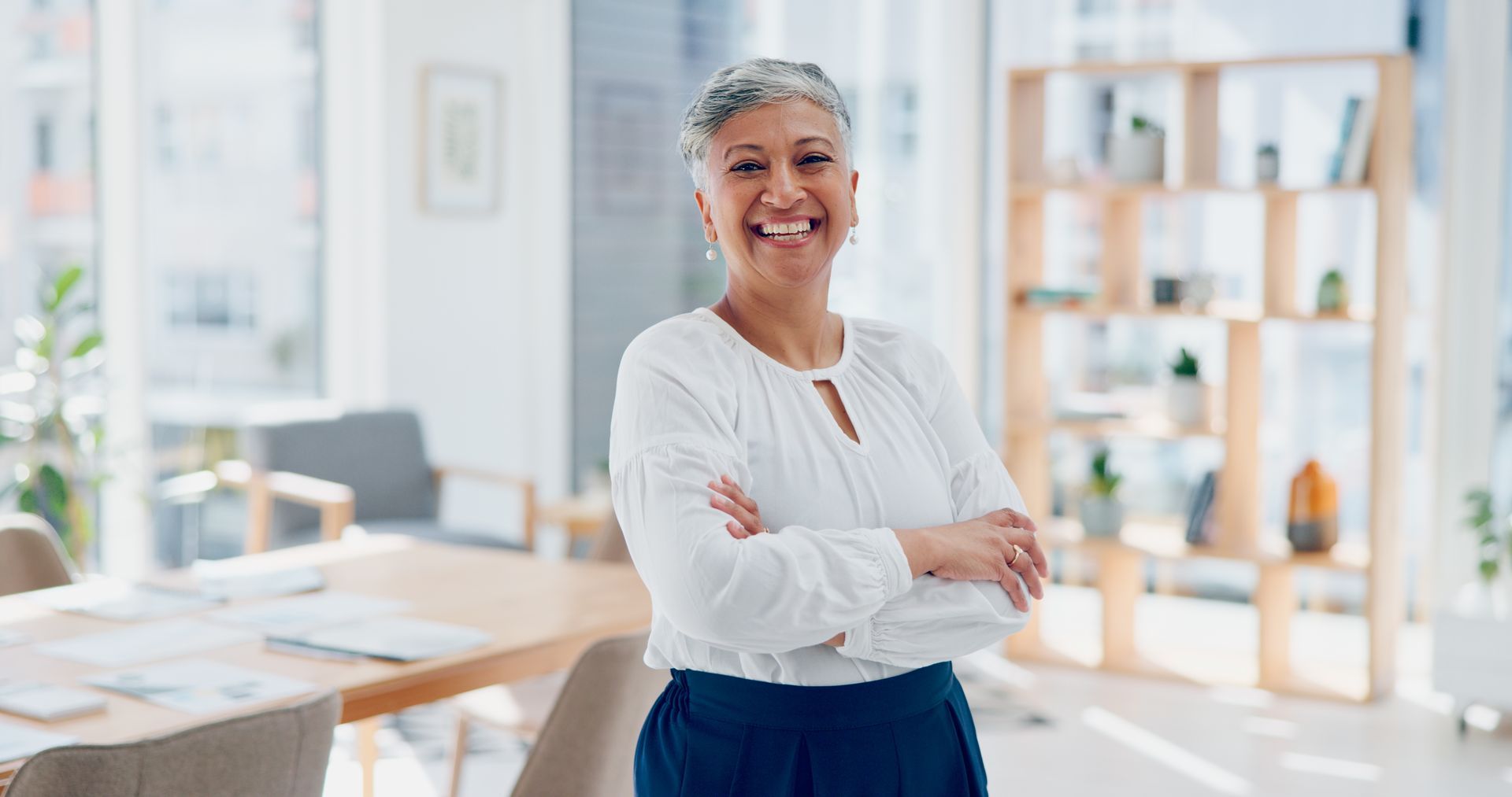 Woman with crossed arms smiles in a well-lit office.